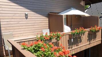 Une terrasse en bois avec une rambarde en bois, un parasol blanc et des fleurs rouges.