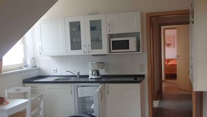 A compact kitchen with white cabinets, a microwave, a coffee maker, and a sink. There is a dining area with a white table and chairs. - Holiday apartment on Blankensee (Trebbin)