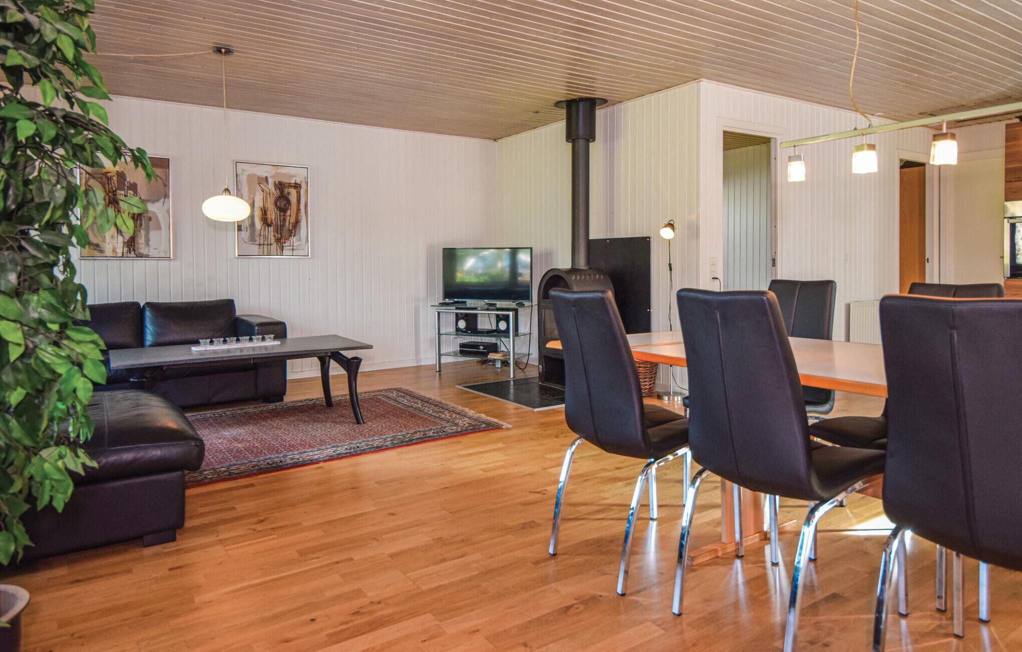 A modern living room with a wooden floor, a black sofa, a dining table with chairs, a TV, and a fireplace.