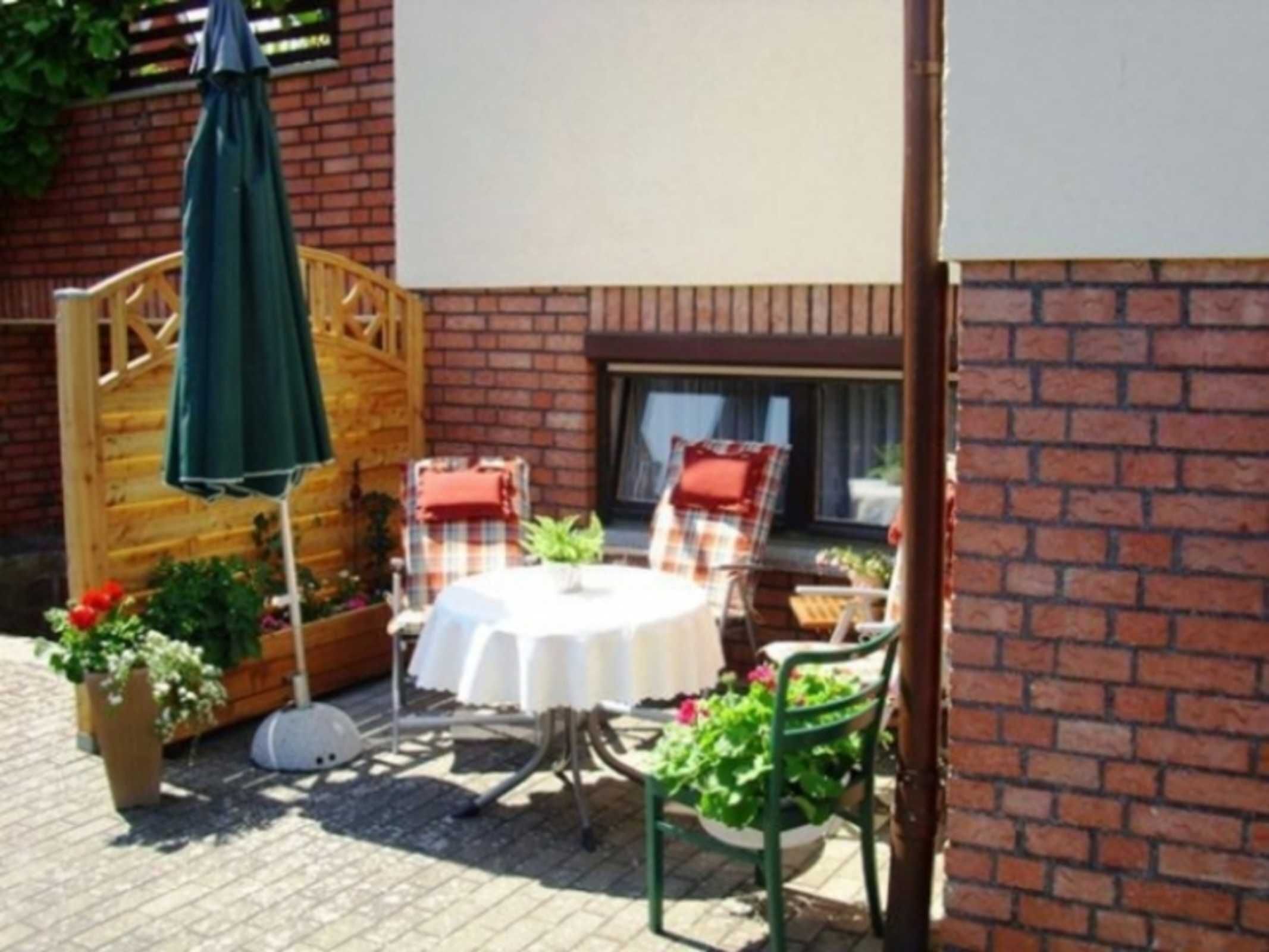 Eine Terrasse im Freien mit einem runden Tisch, zwei Stühlen, einem Holzzaun und Topfpflanzen.