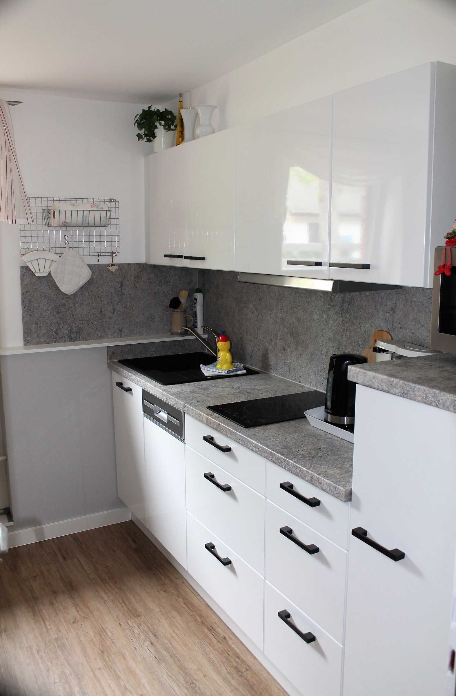 Eine moderne Küche mit weißen Schränken, Granit Arbeitsplatten, einer schwarzen Spüle und einer Kaffeemaschine.
