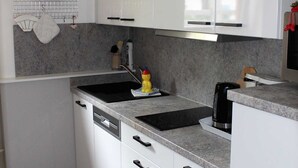 A modern kitchen with white cabinets, granite countertops, a black sink, and a coffee maker. - FeWo Weber - GM 69911 - FeWo Weber (Graal-Müritz)