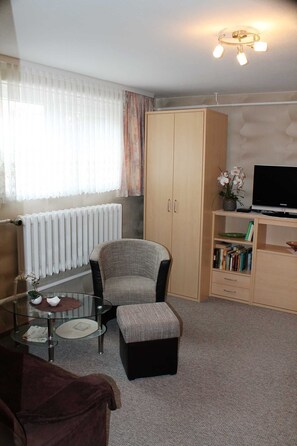Una habitación con sofá, sillón, una mesita, una estantería, un radiador y televisor.