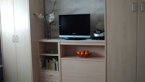 A room with a wooden desk, a television, a vase with flowers, and a bowl of oranges. - FeWo Weber - GM 69911 - FeWo Weber (Graal-Müritz)