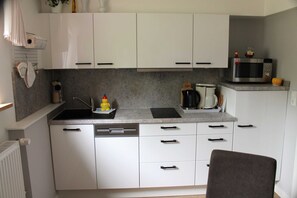 Una cocina compacta con armarios blancos, un microondas y un lavamanos.