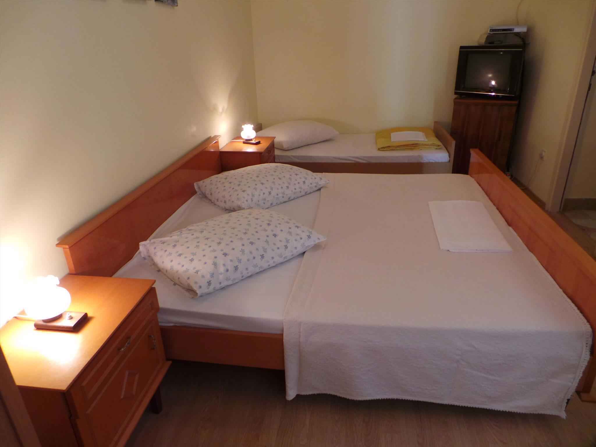 A single bed with two pillows, a bedside table with a lamp, and a television on a stand.