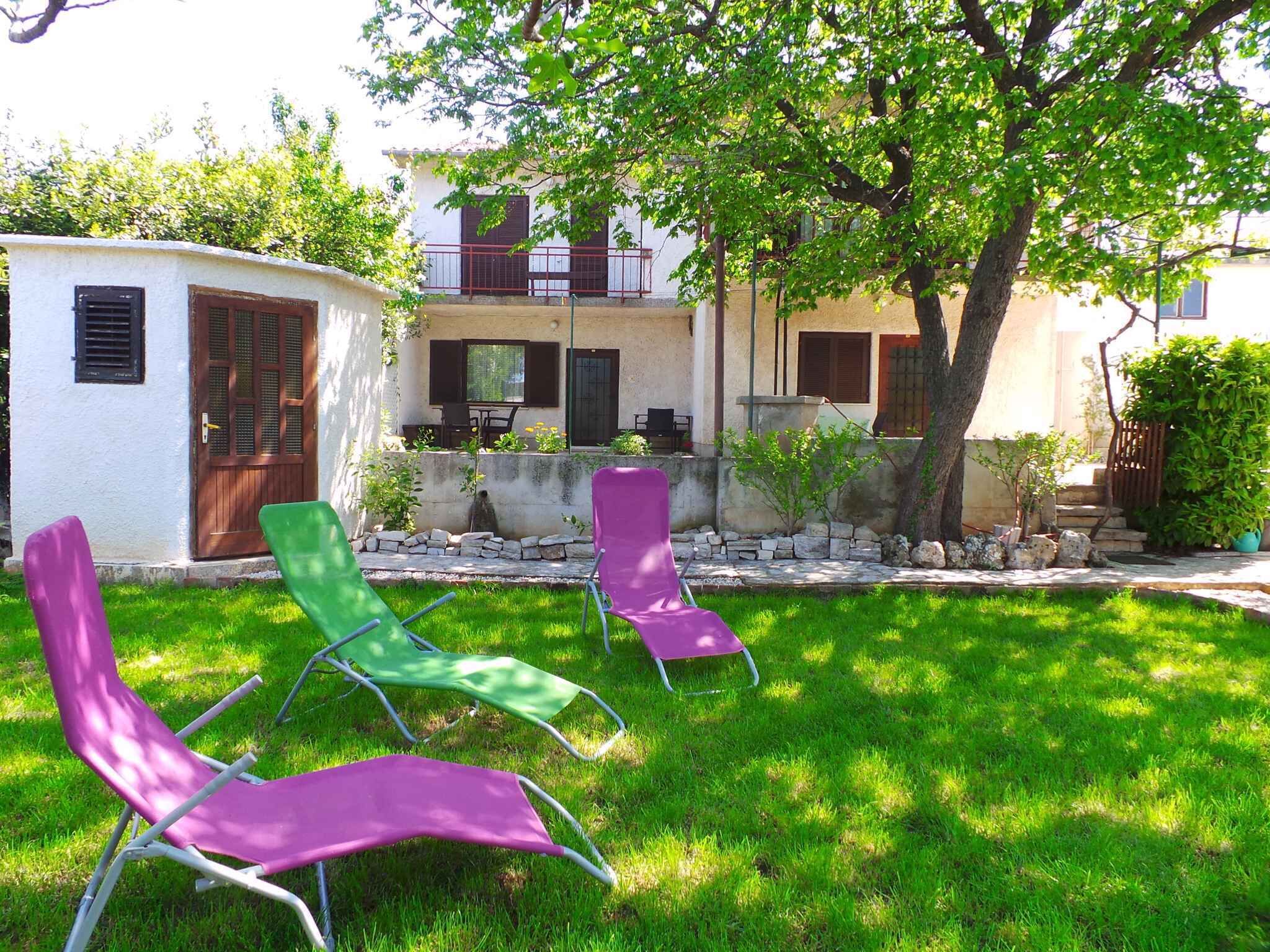 A courtyard with three lounge chairs, a small white building, and a tree providing shade.
