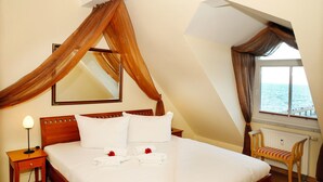 A bedroom with a large bed, a wooden nightstand, a chair, a window with curtains, and a view of the sea. - (60) 3-room apartment with balcony - direct lake view - apartment house (Kühlungsborn)