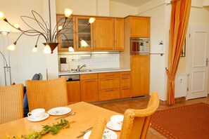 Une cuisine moderne avec des meubles en bois, un four encastré et un coin repas agrémenté de chaises en osier et d’une table dressée pour deux personnes.