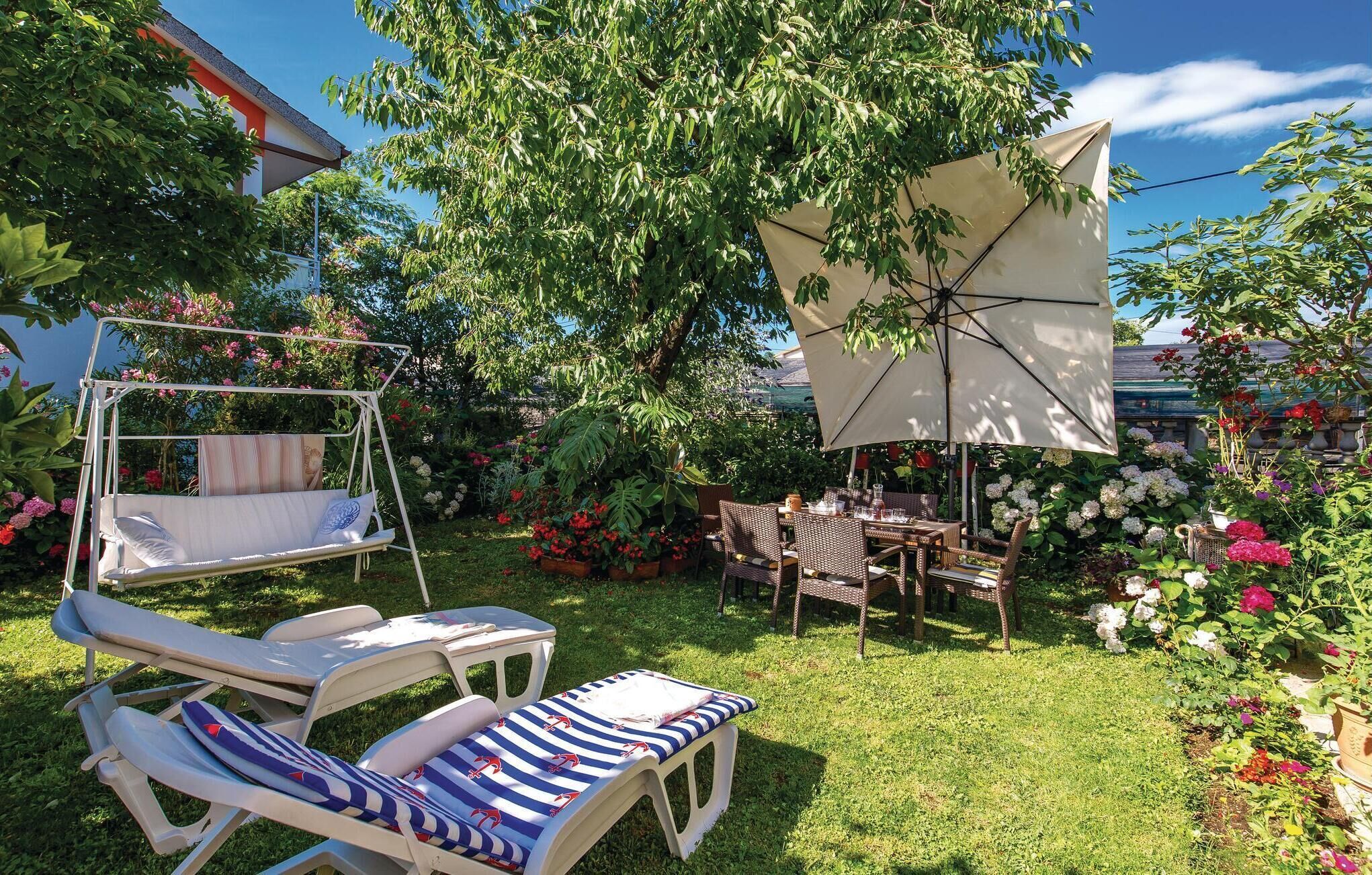Un jardín con una silla mecedora, una mesa con sillas y un gran paraguas que da sombra.