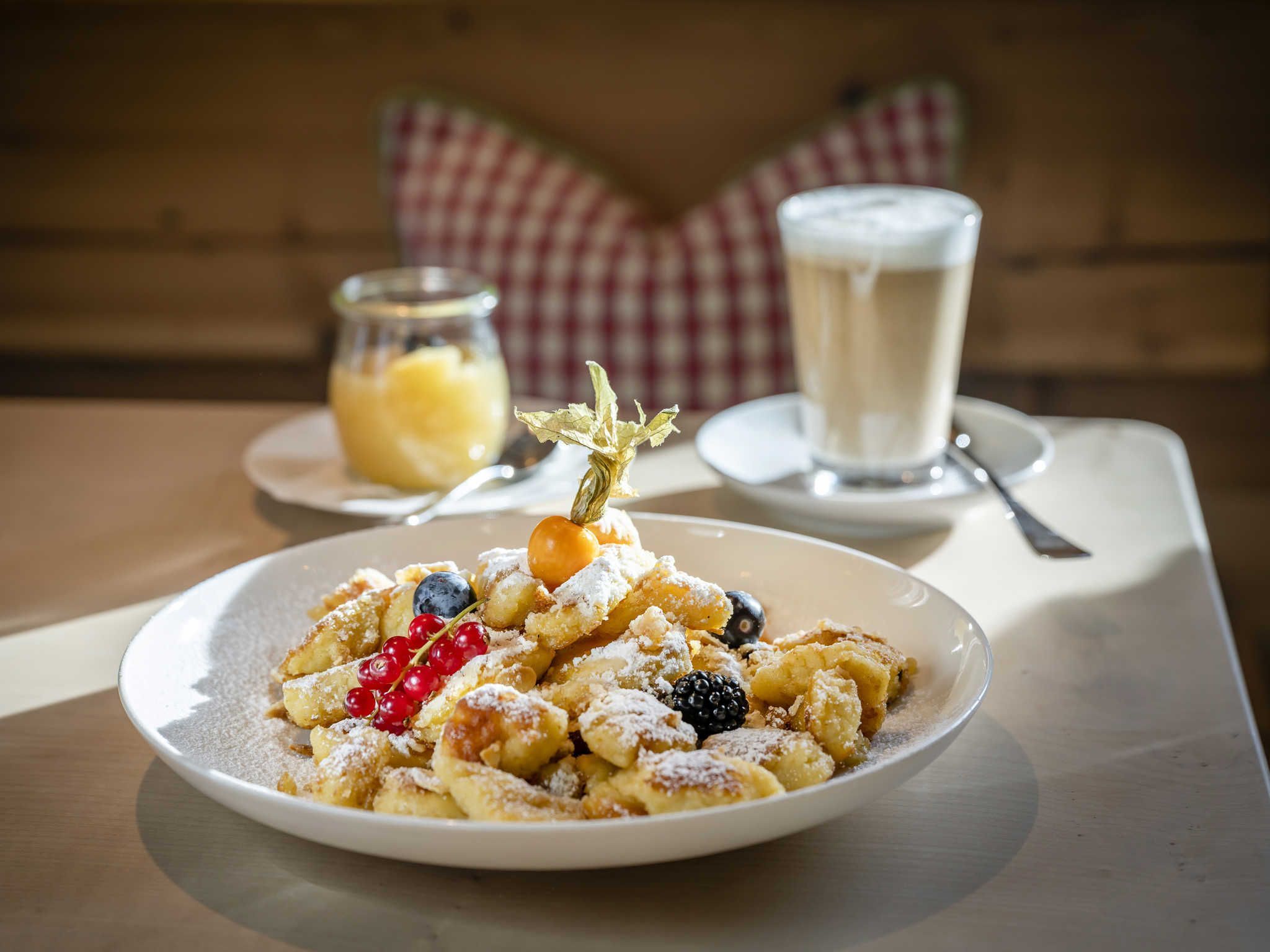 A plate of fritters with berries and powdered sugar, a glass of milk, and a jar of jam on a table.