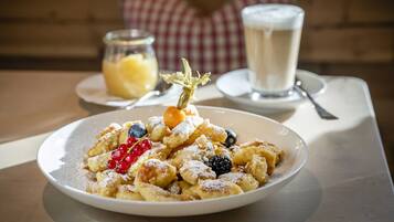 A plate of fritters with berries and powdered sugar, a glass of milk, and a jar of jam on a table.