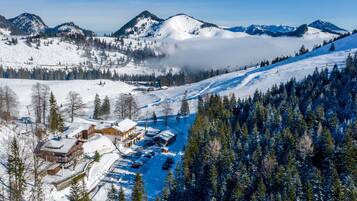 Una località montana innevata con una seggiovia, un'area di parcheggio e un edificio con tetto imbiancato dalla neve.