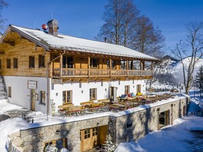A chalet-style building with a wooden balcony, stone lower level, and a snow-covered roof.
