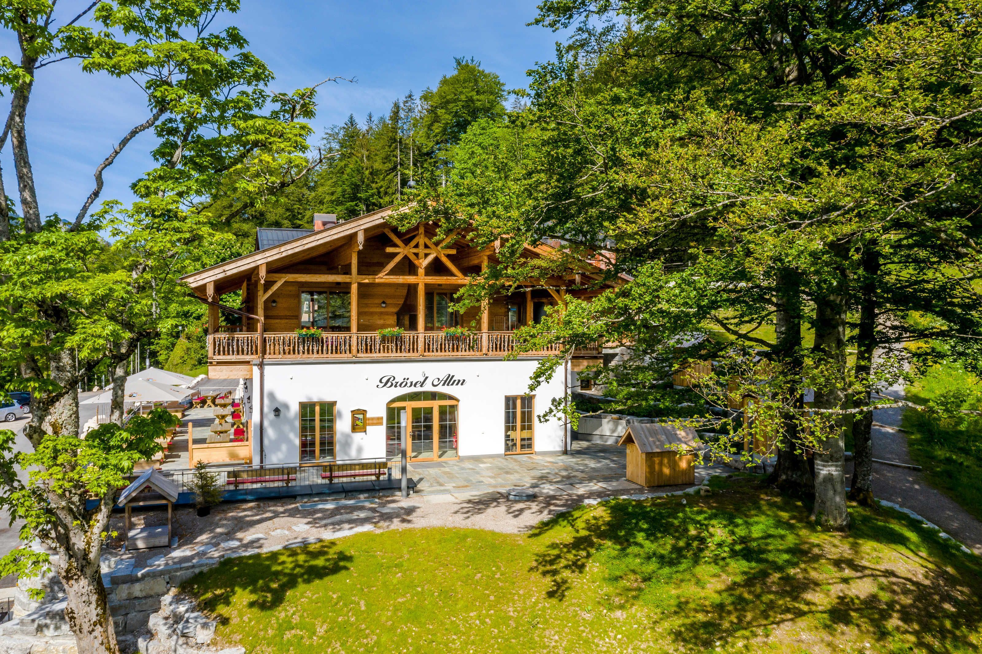 Un edificio in stile chalet con un balcone, un cartello con la scritta 'Bräu Alm' e un vialetto in pietra che conduce all'ingresso.