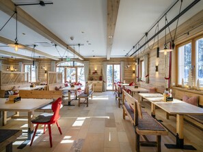 A spacious dining area with wooden tables and benches, large windows, and a high ceiling.