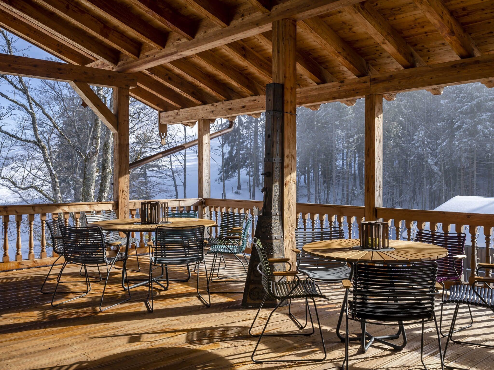 Eine Holzterrasse mit Tischen und Stühlen mit Blick auf einen verschneiten Wald.