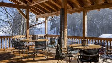 Eine Holzterrasse mit Tischen und Stühlen mit Blick auf einen verschneiten Wald.