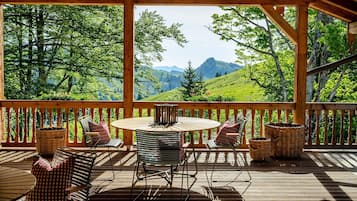 Una terraza de madera con una mesa redonda y sillas, con vistas a un paisaje montañoso.