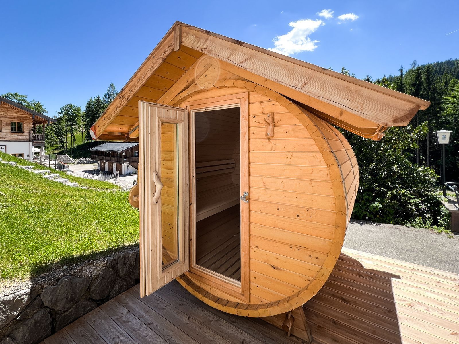 Una sauna in legno con porta aperta, posizionata su un’area pavimentata in legno.