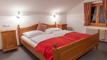 Un letto in legno singolo con una coperta rossa, due comodini, due lampade a parete, una finestra con tende e un termosifone.