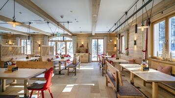 A spacious dining area with wooden tables and benches, large windows, and a high ceiling.