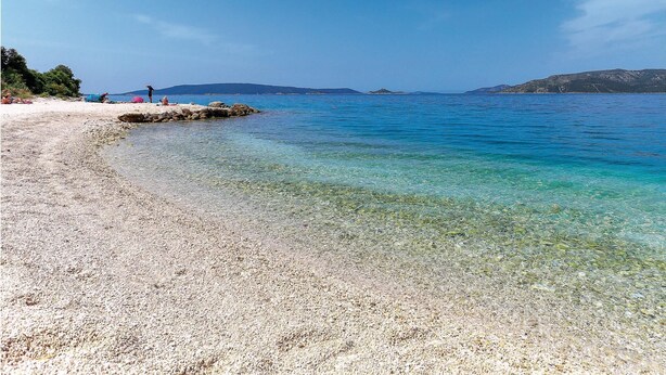 Une plage de galets avec une eau cristalline et des montagnes qui se dessinent à l’horizon.