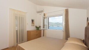 Une chambre à coucher avec un lit, une commode, une fenêtre donnant sur la ville et les collines, et une plante en pot.