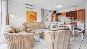 Una sala de estar con muebles de mimbre, una mesa de comedor y una zona de cocina con armarios rojos.