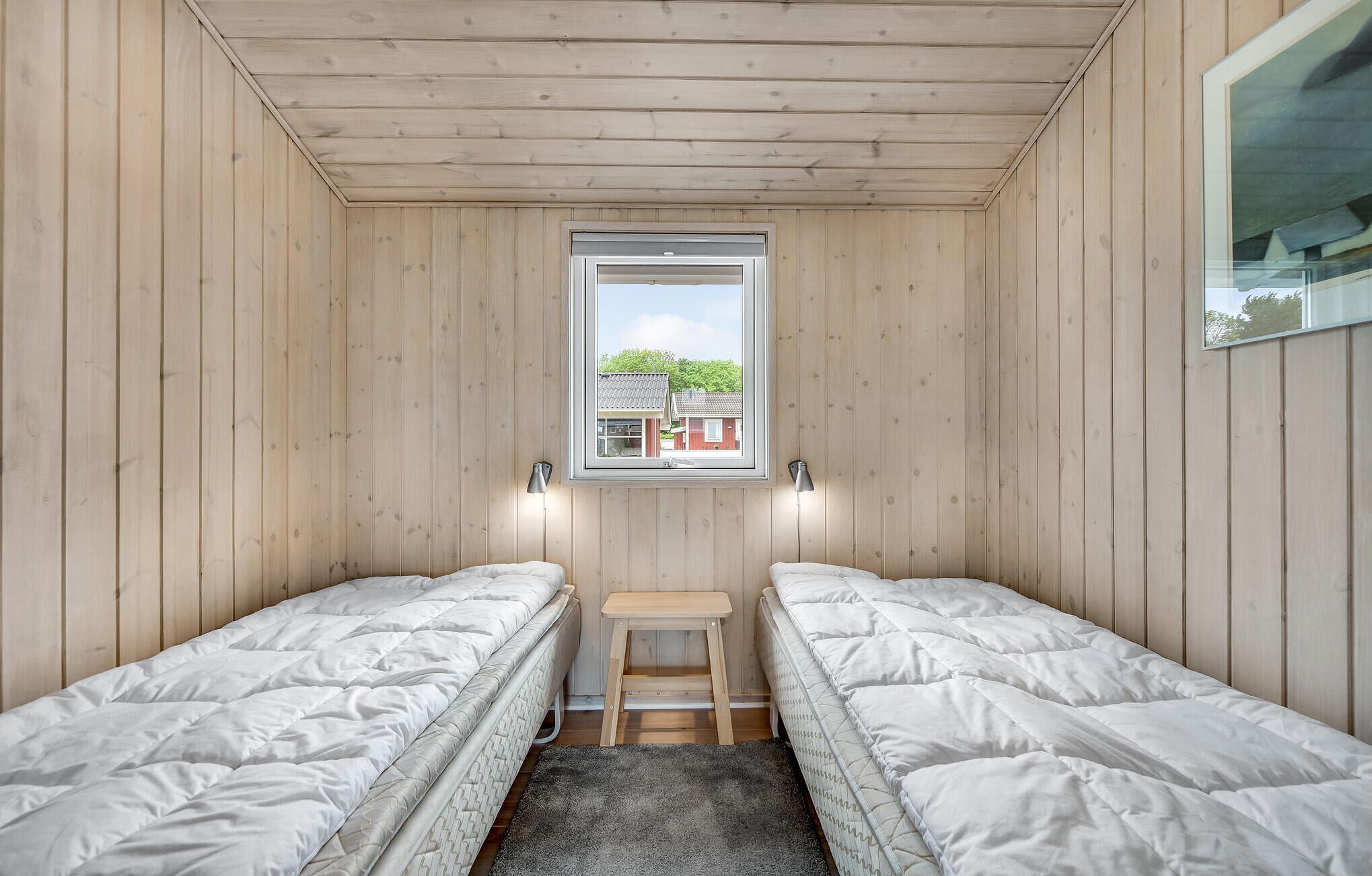 A small, wooden-paneled room with two single beds, a small table, and a window with a view of houses.