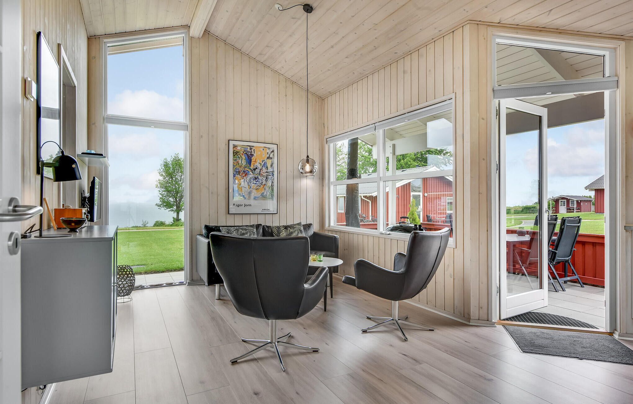 Ein modernes Interieur mit Holzbalkendecke, einem Essbereich mit schwarzen Stühlen, einem Bild an der Wand und Blick auf ein rotes Gebäude im Freien.