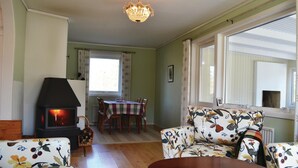 A cozy living room with a fireplace, floral-patterned sofa, wooden dining table, and large windows. - Nice home in Lenhovda with WiFi (Lenhovda)