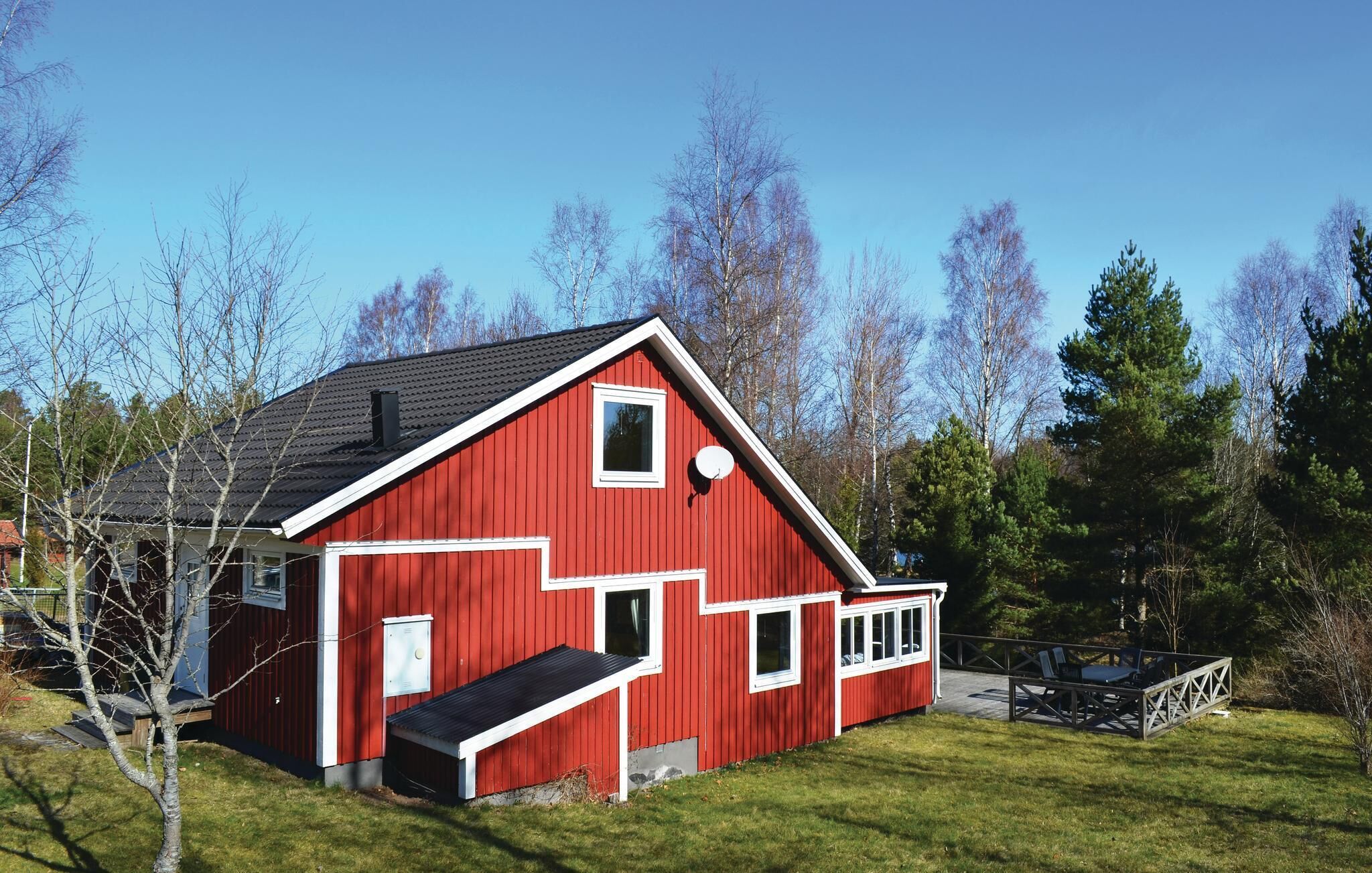 Ein rotes Bauernhaus mit geneigtem Dach, einer kleinen Veranda und einer Terrasse mit Stühlen.