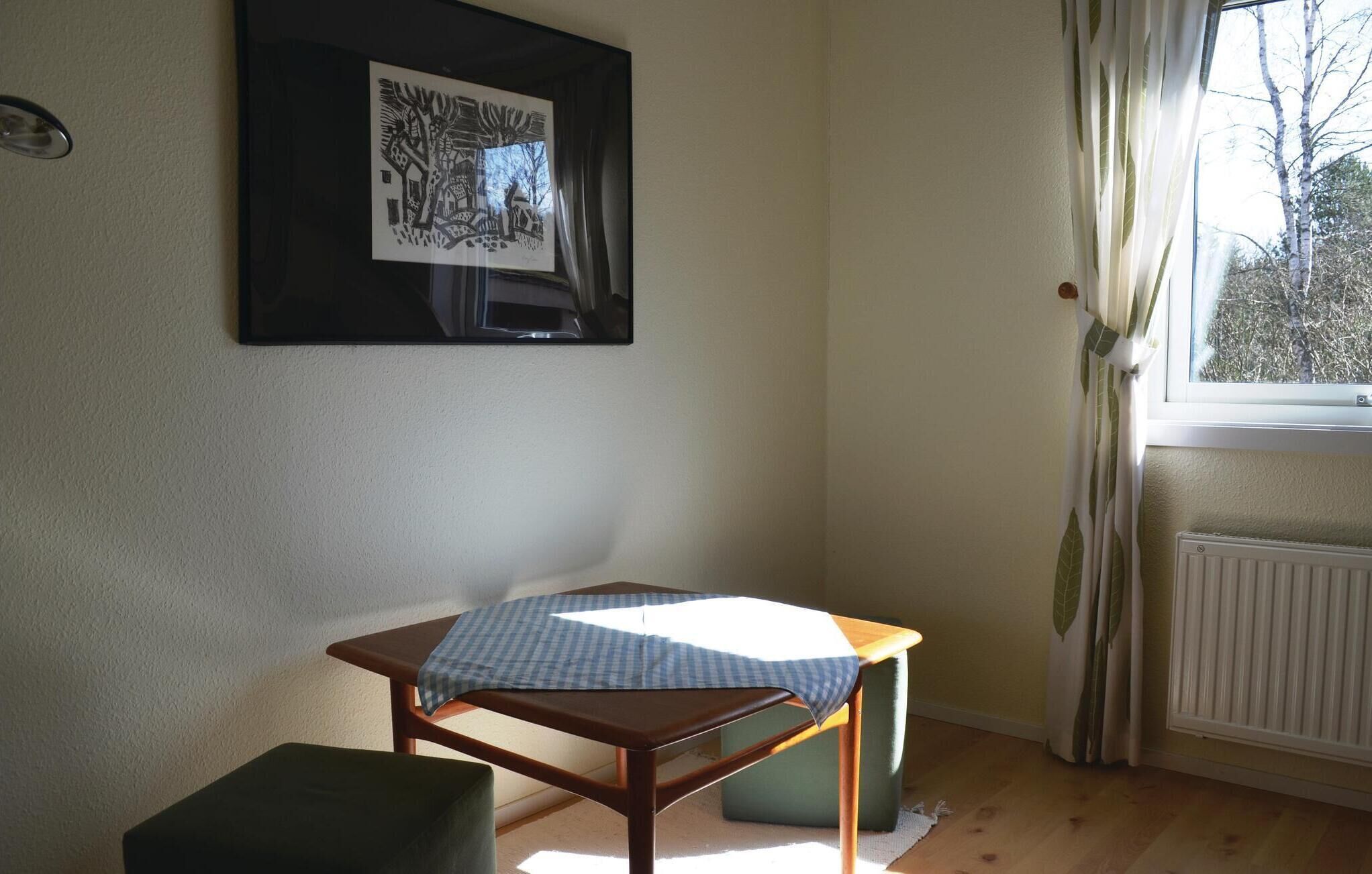Une pièce avec une table, une chaise, un tableau encadré au mur et une fenêtre avec des rideaux.