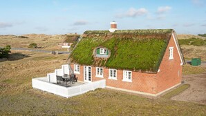 Une maison avec un toit végétalisé, une petite dépendance attenante dotée d’une fenêtre et une clôture blanche en bois.