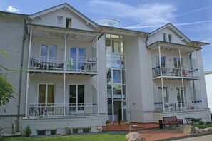 A two-story building with balconies, a covered entrance, and a small outdoor seating area.