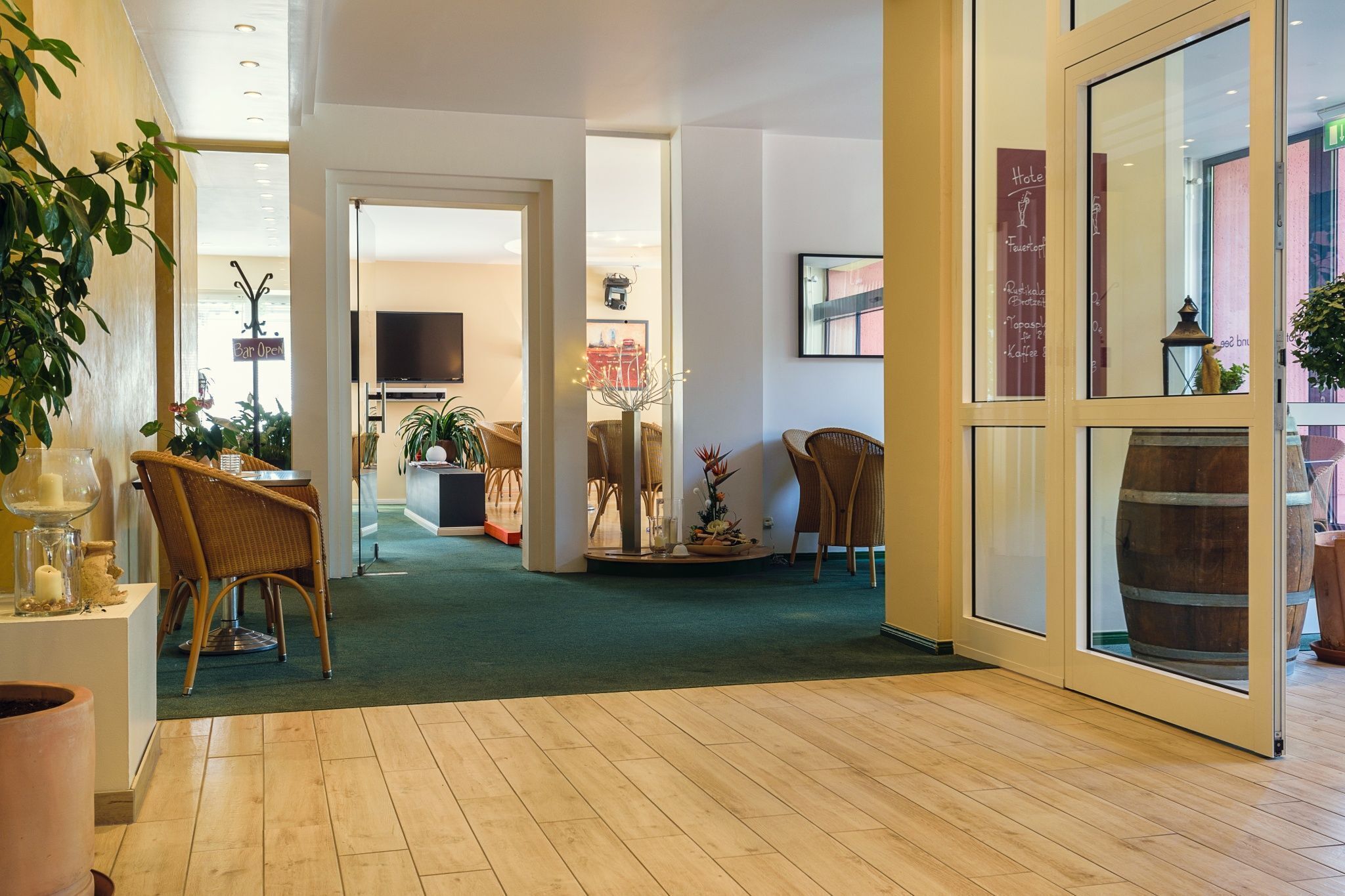 Un hall de hotel con alfombra verde, sillas de mimbre, un arreglo floral central y un ventanal con vistas.