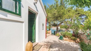 A white building with a green door and windows, a gravel path leading to the entrance, and a view of a body of water in the background. - 1 bedroom beautiful home in Zdrelac (Zdrelac)
