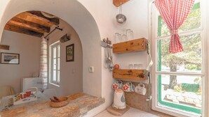 A rustic kitchen with stone countertops, wooden shelves, and a window with a red checkered curtain. - 1 bedroom beautiful home in Zdrelac (Zdrelac)