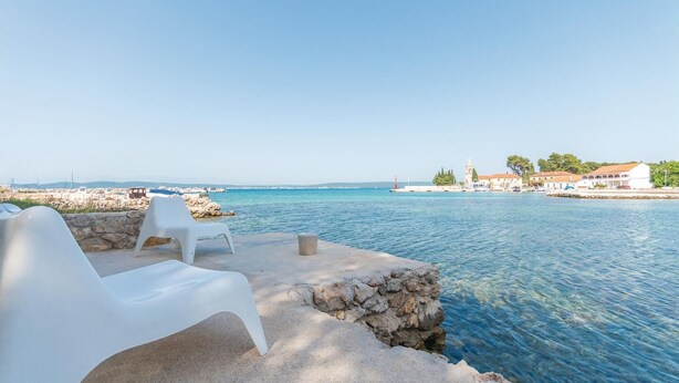 A seaside terrace with white plastic chairs and a stone wall overlooking calm waters. - 1 bedroom beautiful home in Zdrelac (Zdrelac)