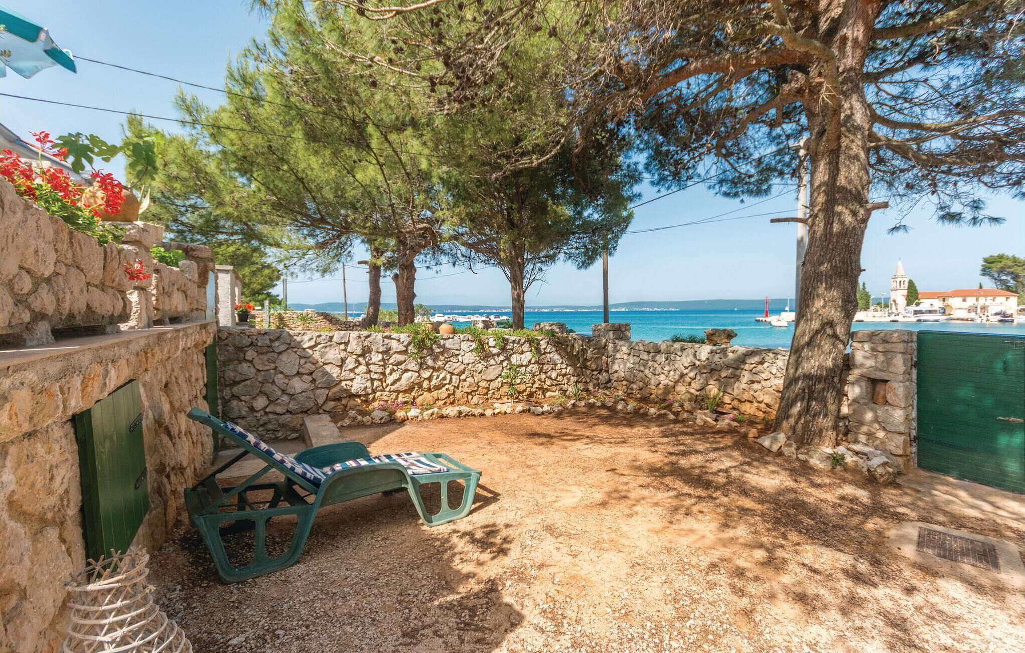 A stone wall with a small table and chairs, a view of the sea, and a building with a red tower in the background.