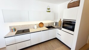 Een moderne keuken met witte kasten, een granieten aanrecht, een spoelbak, een fornuis en een hangmandje.