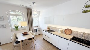 Een moderne keuken met witte kasten, een houten eettafel en een raam met gordijnen.