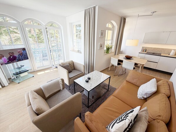 Un salon moderne comprenant un canapé, un fauteuil et une table basse, un coin repas avec une table et des chaises, et une petite cuisine.