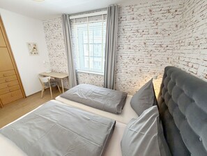 Une chambre avec un mur décoré d’un motif en briques, un bureau et un lit avec une literie grise.