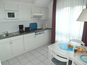 A kitchen with white cabinets, a stove, a sink, and a dining table with a blue placemat.