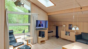 A cozy room with a TV, wooden furniture, a small table, and a view of greenery outside. - 3 bedroom stunning home in Sæby (Sæby)