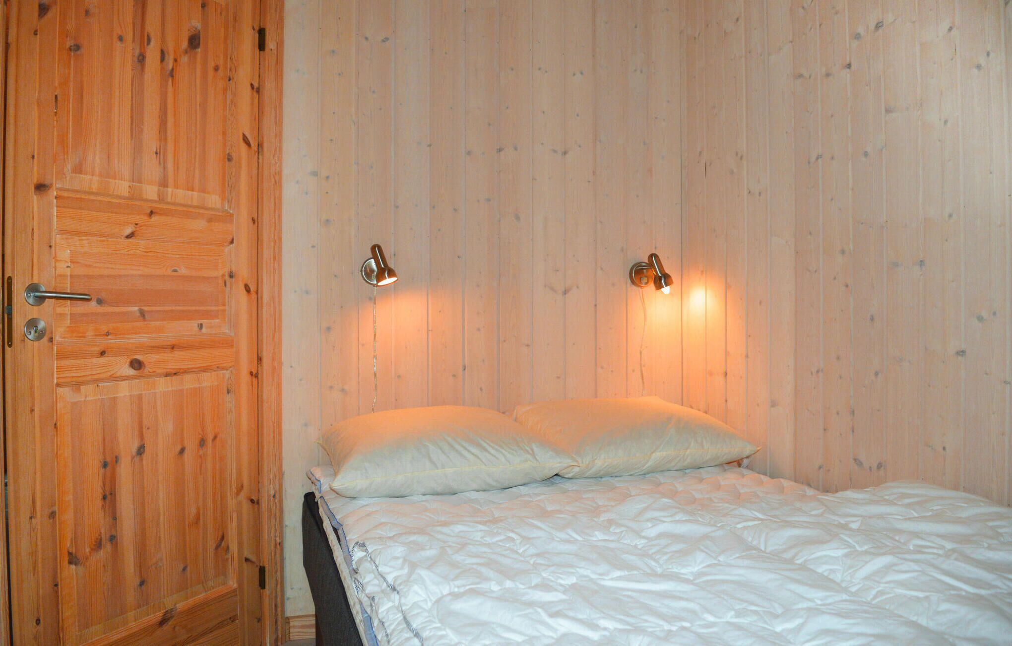 A bedroom with a wooden door, two wall-mounted lamps, and a bed with white bedding.