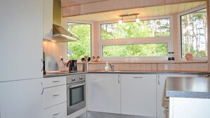 A modern kitchen with white cabinets, a built-in oven, a coffee maker, and a window with a view of trees. - 3 bedroom stunning home in Sæby (Sæby)