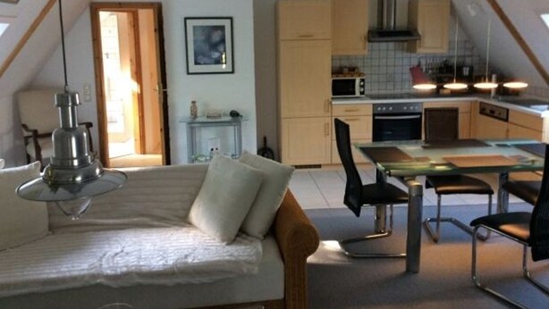 A cozy loft-style bedroom with a bed, a desk, and a chair. A kitchenette with cabinets and a microwave is visible in the background. - Marc Chagall apartment - Rosengut Falkenstein (Braderup)